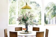 an airy dining room with a round table, antique chairs with floral upholstery and a yellow pendant lamp is a lovely and cozy space
