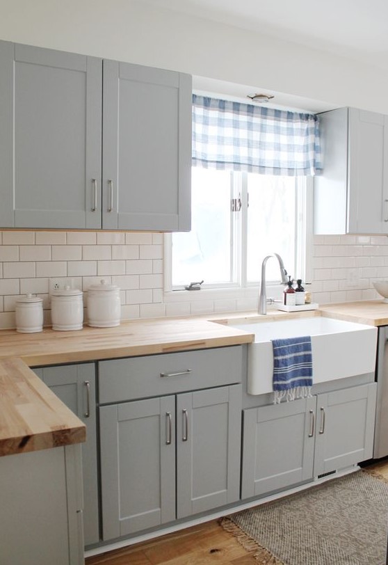 an airy kitchen with dove grey cabinets, a white subway tile backsplash and wooden cuntertops looks cool and bold