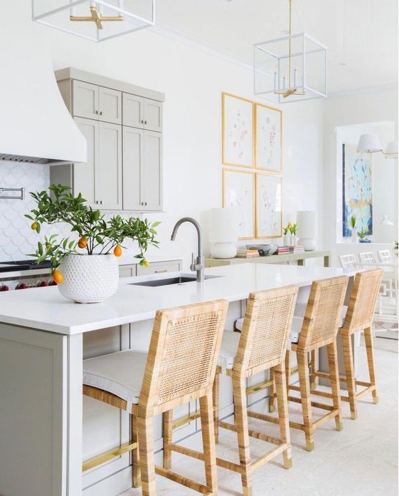 an airy kitchen with dove grey cabinets and a kitchen island, white stone countertops, wicker stools and frame chandeliers