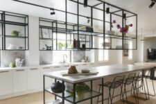 an airy kitchen with white cabinets and a large kitchen island, black metal and glass suspended shelves and ablack stools