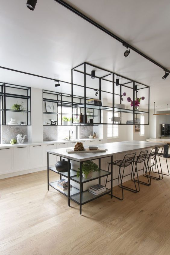 an airy kitchen with white cabinets and a large kitchen island, black metal and glass suspended shelves and ablack stools