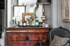 an antique nook with a stained dresser, some artwork and mirrors, a black antique chair, a black table lamp and a leopard print pillow