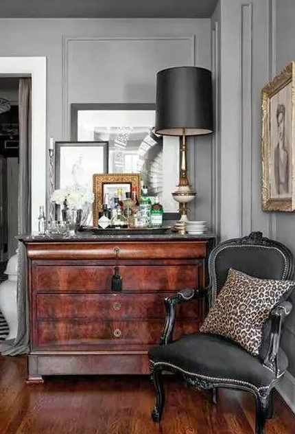 an antique nook with a stained dresser, some artwork and mirrors, a black antique chair, a black table lamp and a leopard print pillow