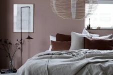 an attic bedroom with a mauve accent wall, green and rust bedding and a stick lamp looks very calming and soothing