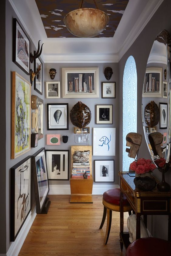 an awkward nook turned into an art-filled space with a floor to ceiling gallery wall that takes two walls, a vintage console table and a round mirror