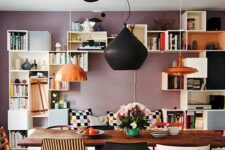 an eclectic dining room with a mauve accent wall, lots of open shelves, a banquette seating, a wooden table and mismatching chairs