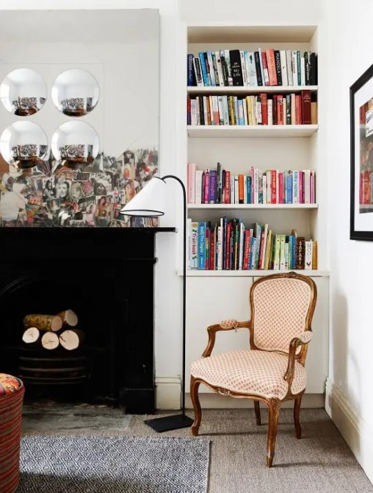 an eclectic living room with a black non-working fireplace, built-in bookshelves, a series of mirrors and an antique chair redone with polka dot upholstery