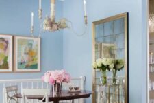 an eclectic pastel blue dining room with a vintage mirror, a stained table and white chairs, a chandelier suspended on rope