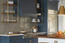 an elegant blue kitchen with a glossy grey tile backsplash, suspended brass shelves, brass pendant lamps and stools