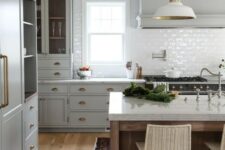 an elegant light grey kitchen with chic gold handles, a white subway tile backsplash, white countertops and white pendant lamps