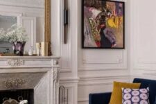 an exquisite living room with a French fireplace, a navy sofa with bold pillows, a bright artwork and layered coffee tables