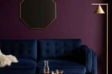 an exquisite living room with a deep purple accent wall, a navy sofa, a beautiful wooden coffee table and a gold floor lamp