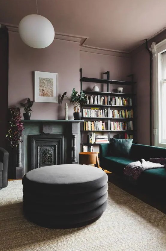 an exquisite living room with mauve walls and a ceiling, open shelves, a green sofa, a non-working fireplace and potted plants