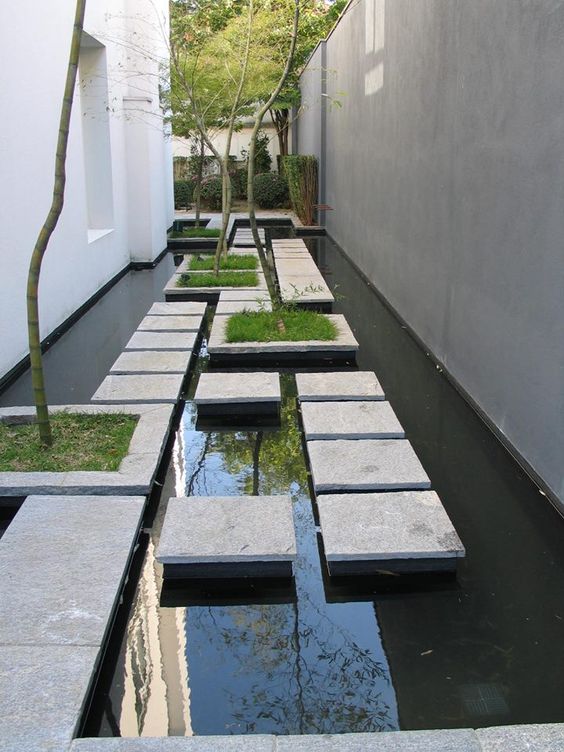 a minimalist outdoor space with a large pond, with tiles floating over the water, with some planted greenery and trees