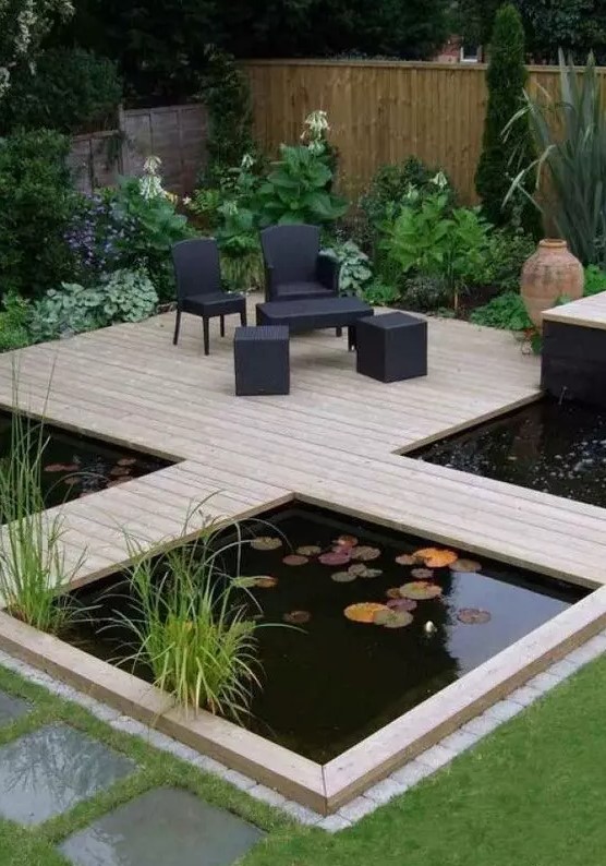 a modern garden with green lawn and some blooms, a wooden deck with black outdoor furniture, a couple of ponds