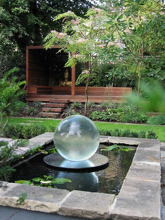 a modern pond clad with large pieces of stone, with water plants and a glass sphere in the center of the pond looks cool