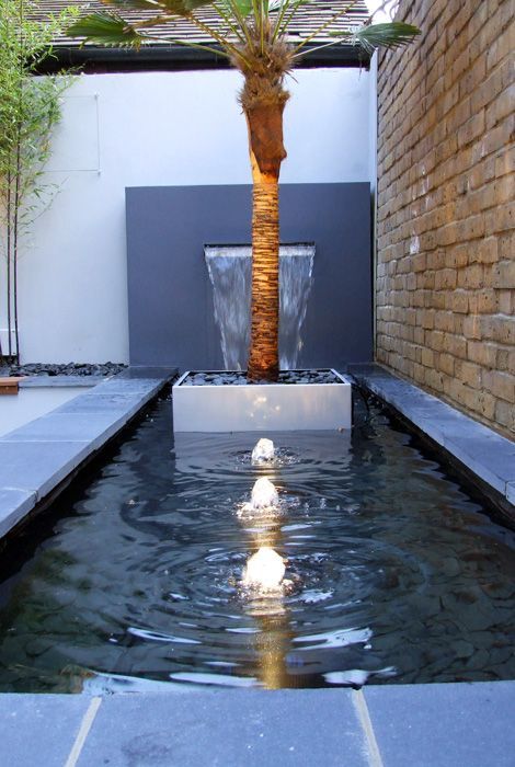 a modern pond with built in lamps and fountains, with a planted tree and a waterfall is a cool and catchy combo for any modern garden