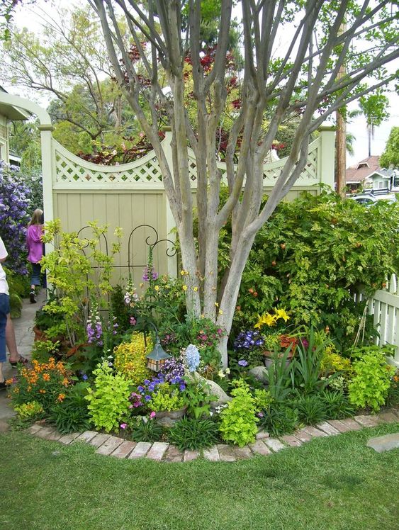 a tree with a garden bed with greenery and bright flowers right around it is a super cool idea for a bold garden