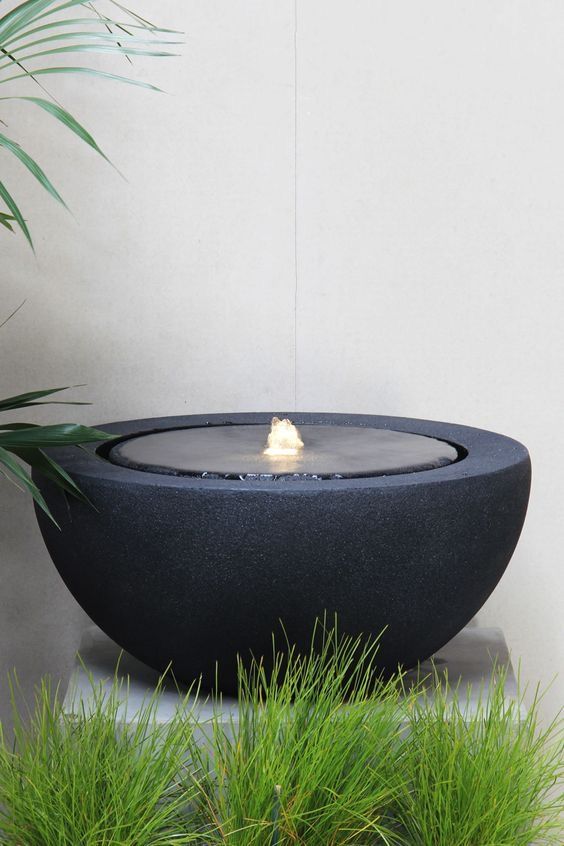 a modern outdoor fountain of a large black bow surrounded with greenery is a catchy and bold solution for a modern space