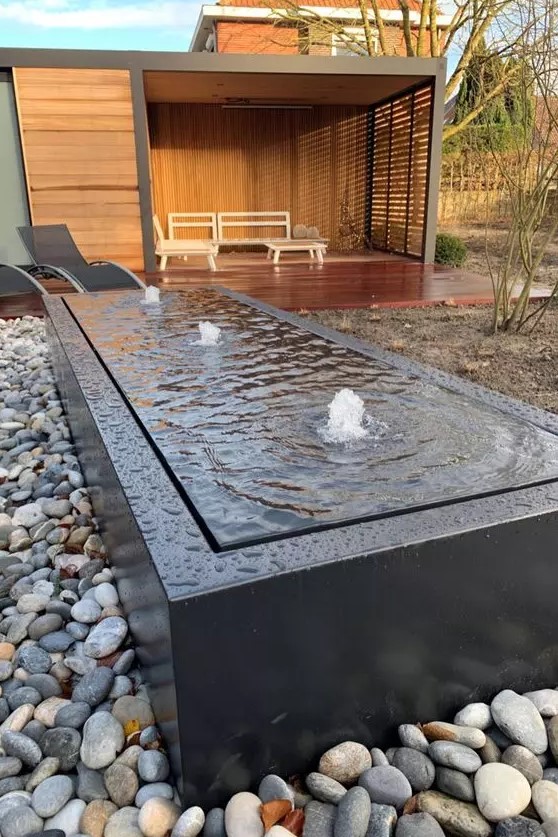 a modern box fountain with a black metal box surrounded with pebbles is a lovely addition to a modern garden space
