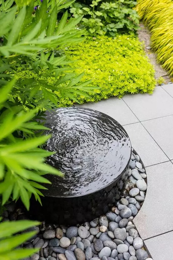 a modern bowl fountain surrounded with pebbles and super bold grasses and grasses is a lovely idea for a modern garden