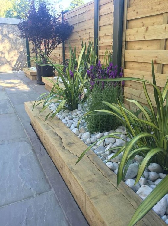 a wooden garden bed edge, bright flowers and greenery all covered with neutral pebbles on top
