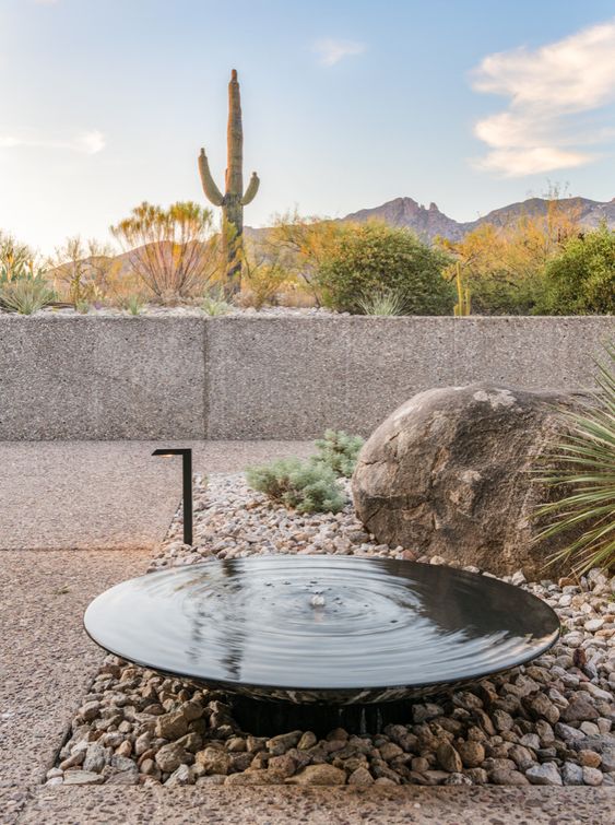 a large metal bowl placed on large rocks is a cool outdoor water feature and decor idea to rock, it will be a nice idea for a desert garden