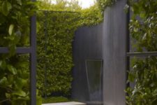 29 a minimalist outdoor space with greenery walls, a black wall with a waterfall flowing into a water feature and a white tile deck