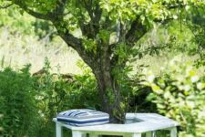 29 a white bench around the tree, with a striped pillow, is a lovely spot to have a seat in your garden, very secluded and cozy