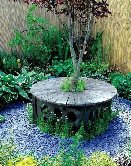 an elegant carved stained bench around the tree, with pebbles and blooms around is a lovely sitting spot for your garden