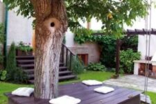 31 a dark deck around the tree with white pillows under the tree is a lovely space that welcomes you to the garden