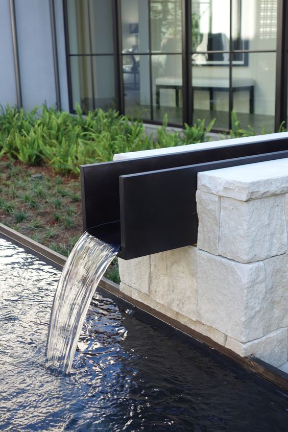 a modern pond paired with an ultra modern waterfall with a black metal piece is a stylish solution for a bold and edgy space