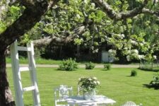 41 a relaxed white dining spot around the tree, with white blooms, a ladder next to the tree is a lovely space for summer
