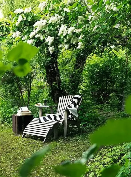 an under the tree mini lounge with a wooden lounger and a crate side table, some blankets and books is amazing