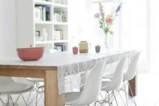a Nordic dining room with a white bookcase, a light-stained wooden dining table, white Eames chairs and pendant bulbs over the space