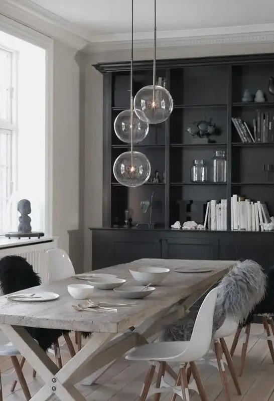 a Nordic dining space with a black storage unit, a reclaimed trestle dining table, white Eames chairs and pendant lamps