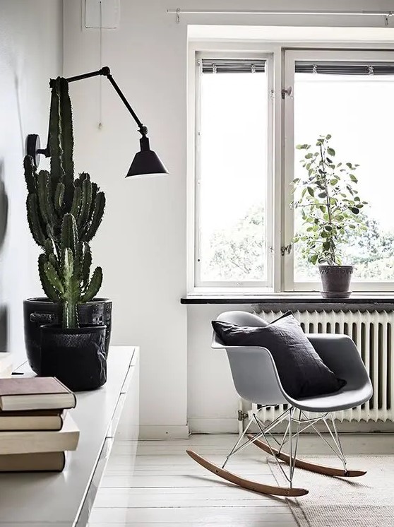 a Nordic room with a white Eames rocking chair, a white credenza with books and a cactus, a black sconce