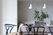 a Scandi dining space with a storage unit and a built-in seat, a dining table and navy wishbone chairs, white pendant lamps