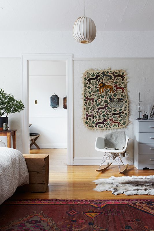 a Scandinavian bedroom with a bed, a wooden slab bench, a console table, a grey dresser, a white Eames rocker and an artwork