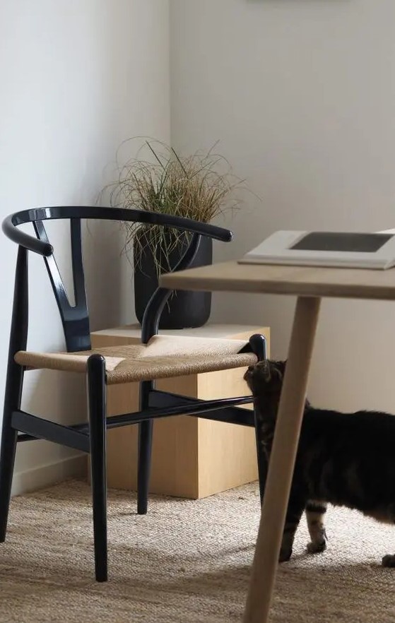 a Scandinavian dining and working space with a light-stained table, a black wishbone chair, a stand with a black plantern and a rug