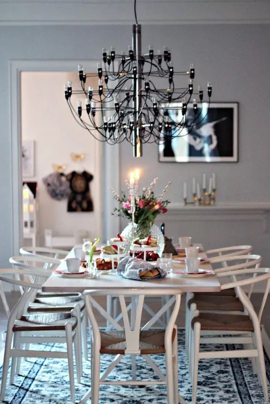 a Scandinavian dining space with a dining table, white wishbone chairs, a black chandelier and a printed rug