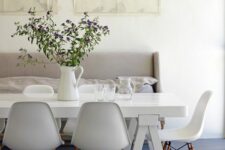 a Scandinavian dining space with a neutral sofa, a white trestle table, white Eames chairs and some maps