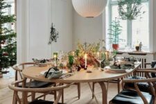 a Scandinavian dining space with a stained table, stained and black wishbone chairs, a white pendant lamp and some Christmas decor