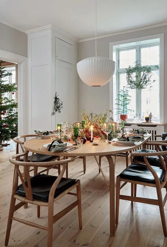 a Scandinavian dining space with a stained table, stained and black wishbone chairs, a white pendant lamp and some Christmas decor