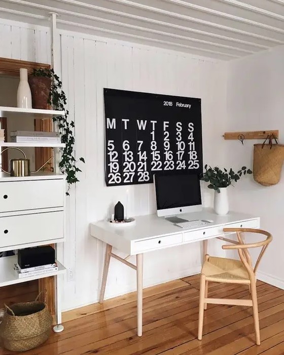 a Scandinavian dining space with a white desk, a light-stained chair, a storage unit, a calendar and some greenery