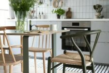a Scandinavian kitchen in light grey, with a green and stained table and a green wishbone chair plus a striped rug