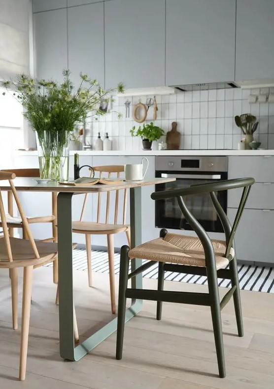 a Scandinavian kitchen in light grey, with a green and stained table and a green wishbone chair plus a striped rug