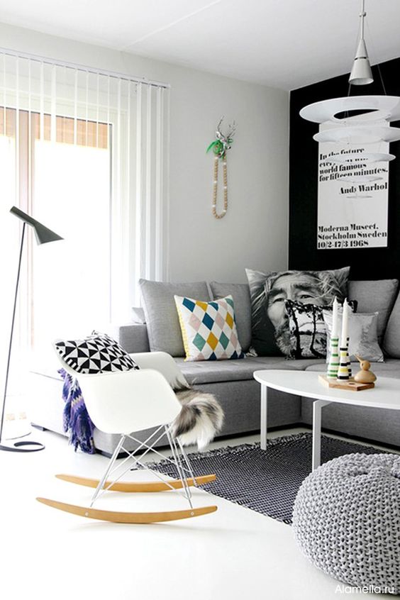 a Scandinavian living room with a black accent wall, a grey sectional, a white coffee table and an Eames rocker plus some printed pillows