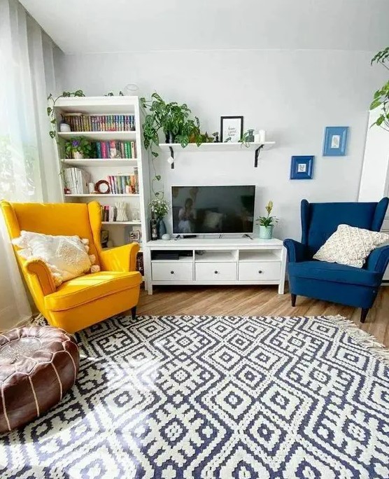 a Scandinavian living room with a bookcase, a TV unit, a navy and yellow Strandmon chair, a printed rug and a leather pouf plus potted greenery