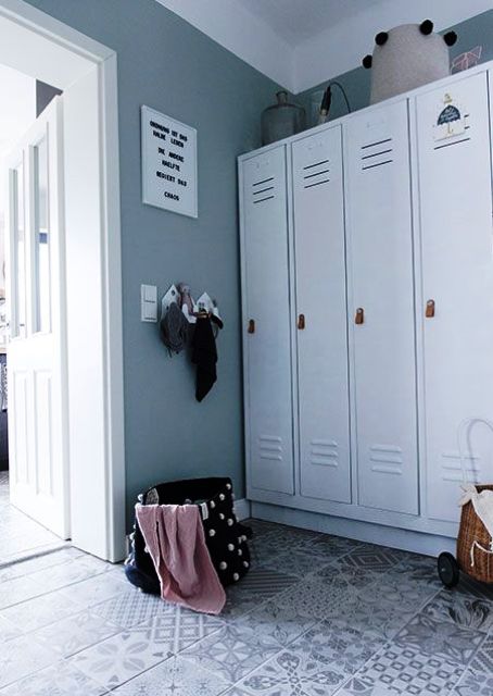 a Scandinavian mudroom in slate grey, with white lockers, a tiled floor, a basket and some decor on the wall